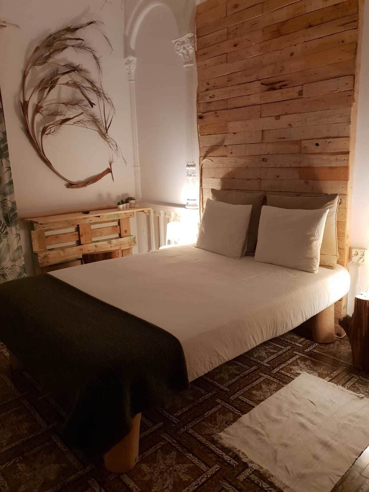 Une chambre à coucher avec une tête de lit en bois, un grand lit avec une literie blanche, un élément décoratif mural et une petite table de chevet.