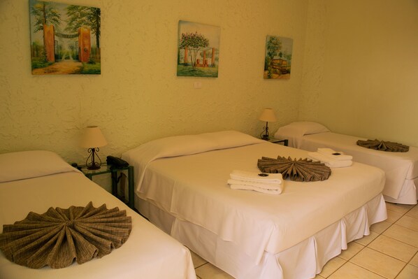 A hotel room with three beds, each with white linens and decorative pillows. There are paintings on the wall and a small table with a lamp and phone. - Hotel Jardim da Serra (São Pedro)