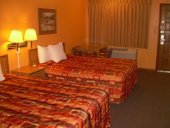 Habitación de hotel con dos camas, un escritorio y una silla. Hay dos lámparas en las mesitas de noche.