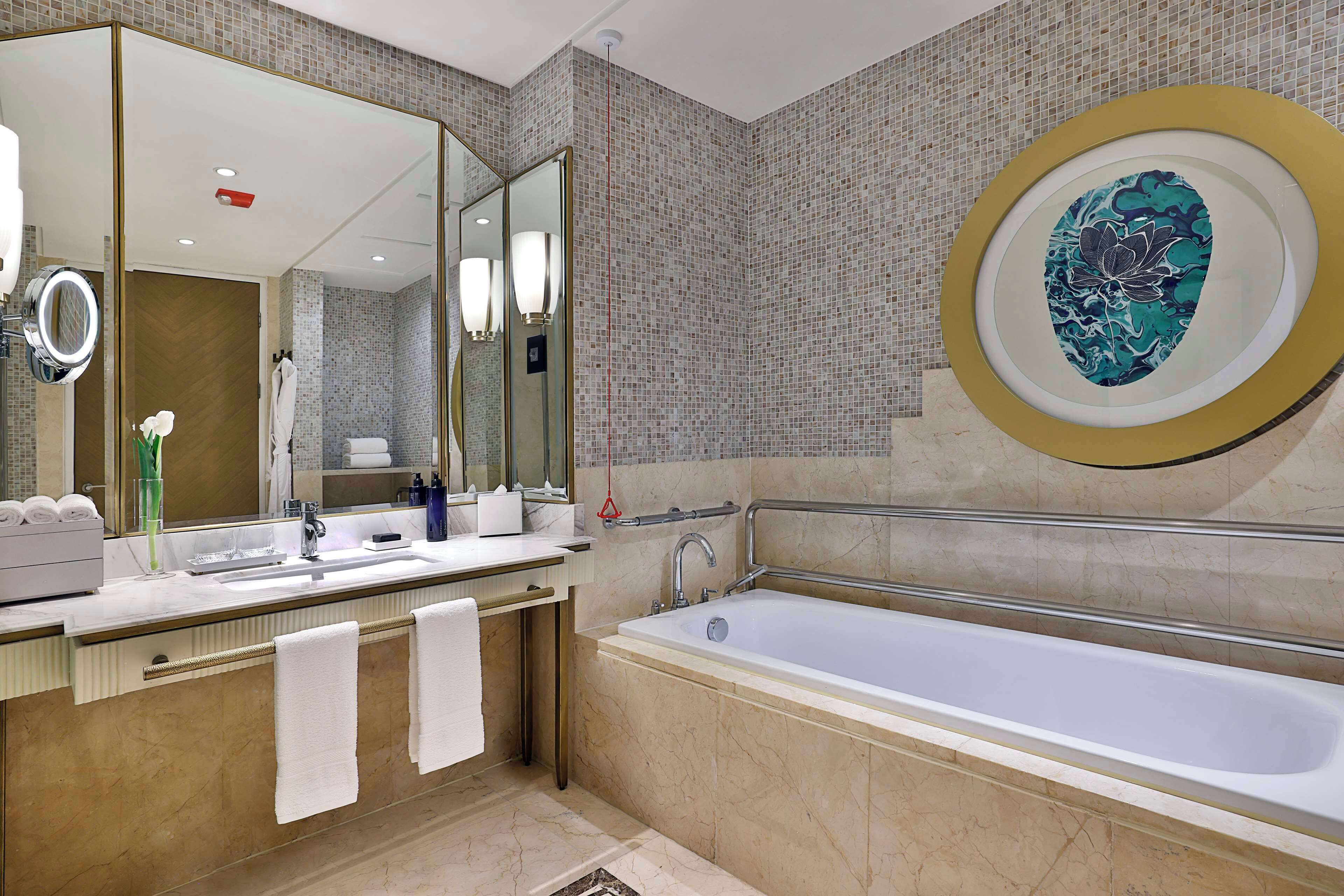 A modern bathroom with a large mirror, a bathtub, and a vanity with a sink and towel rack.