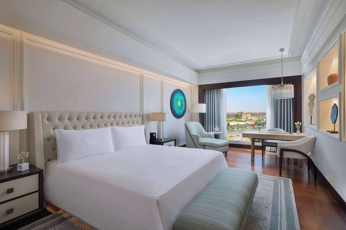 A hotel room with a large bed, a desk, a chair, and a view of the city.