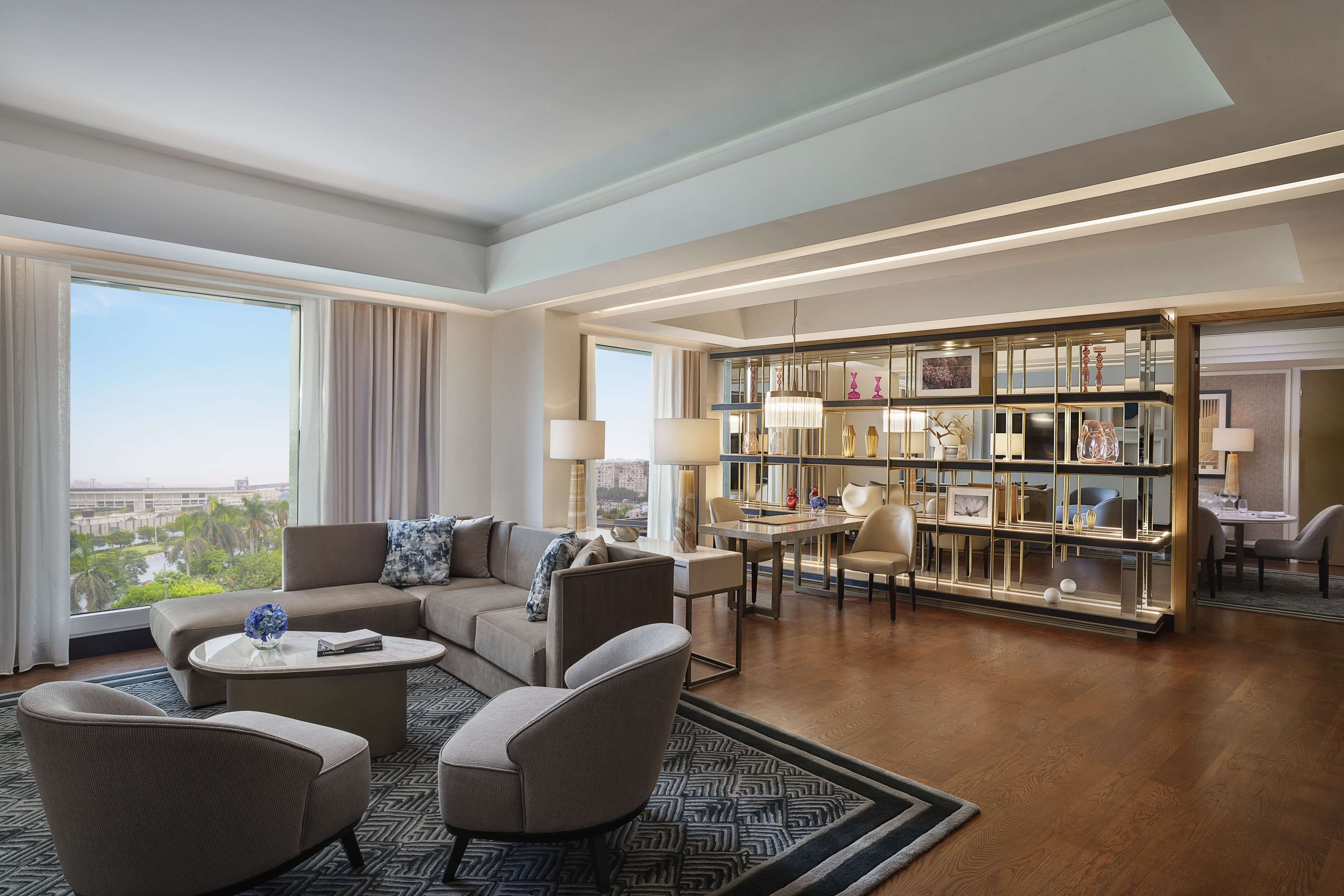 Een ruime woonkamer met een bank, fauteuils, een salontafel en een boekenkast.