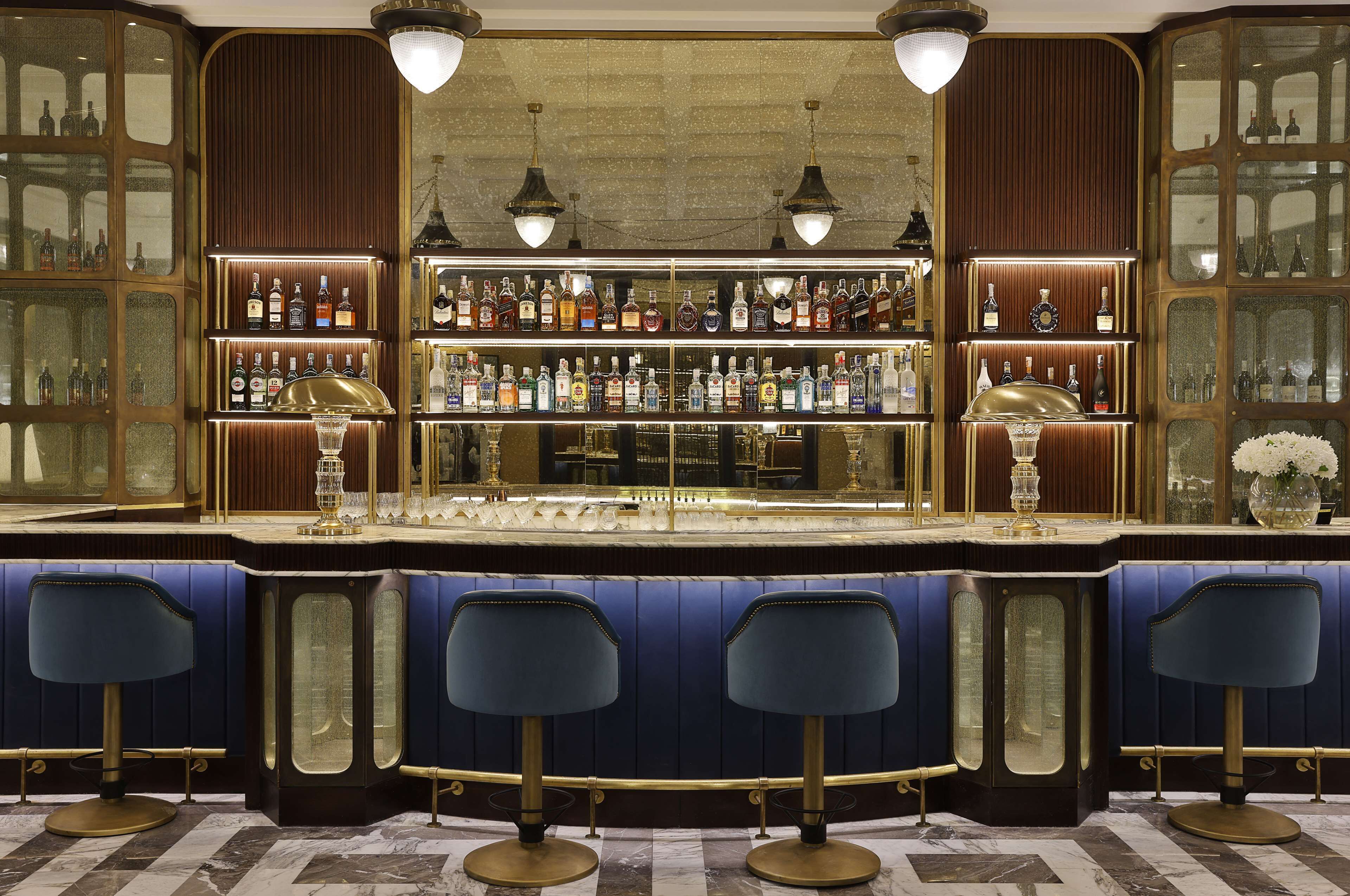 A bar area with a marble floor, bar stools, and shelves of liquor bottles.