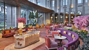 A spacious lobby with a central bar, comfortable seating areas, and large windows offering views of the building's exterior. - Waldorf Astoria Cairo Heliopolis (Cairo)