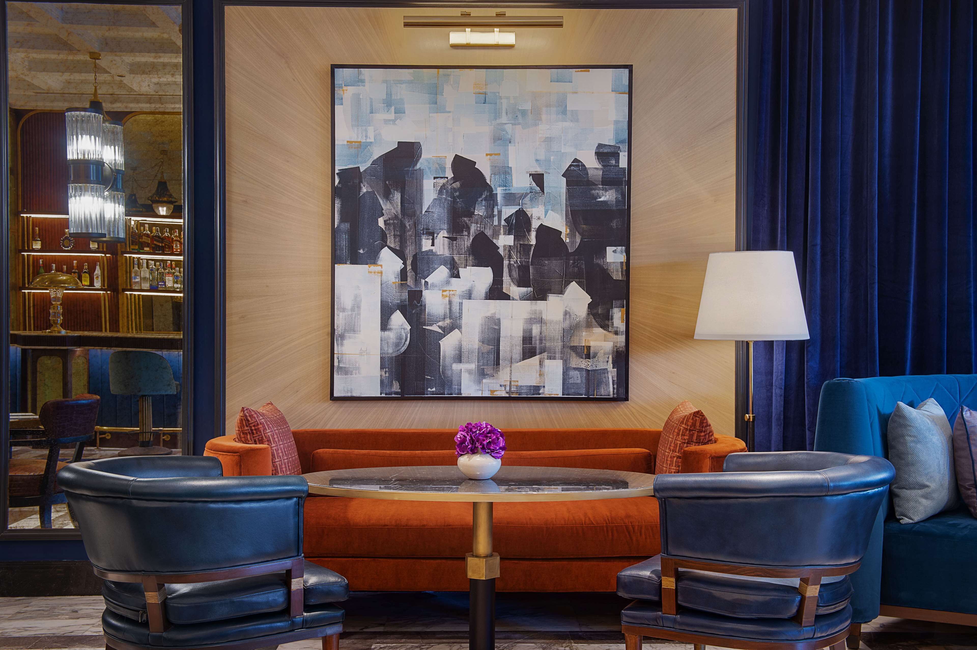 Een moderne lounge met een groot abstract schilderij, lederen zitplaatsen en een bar met flessen op de planken.