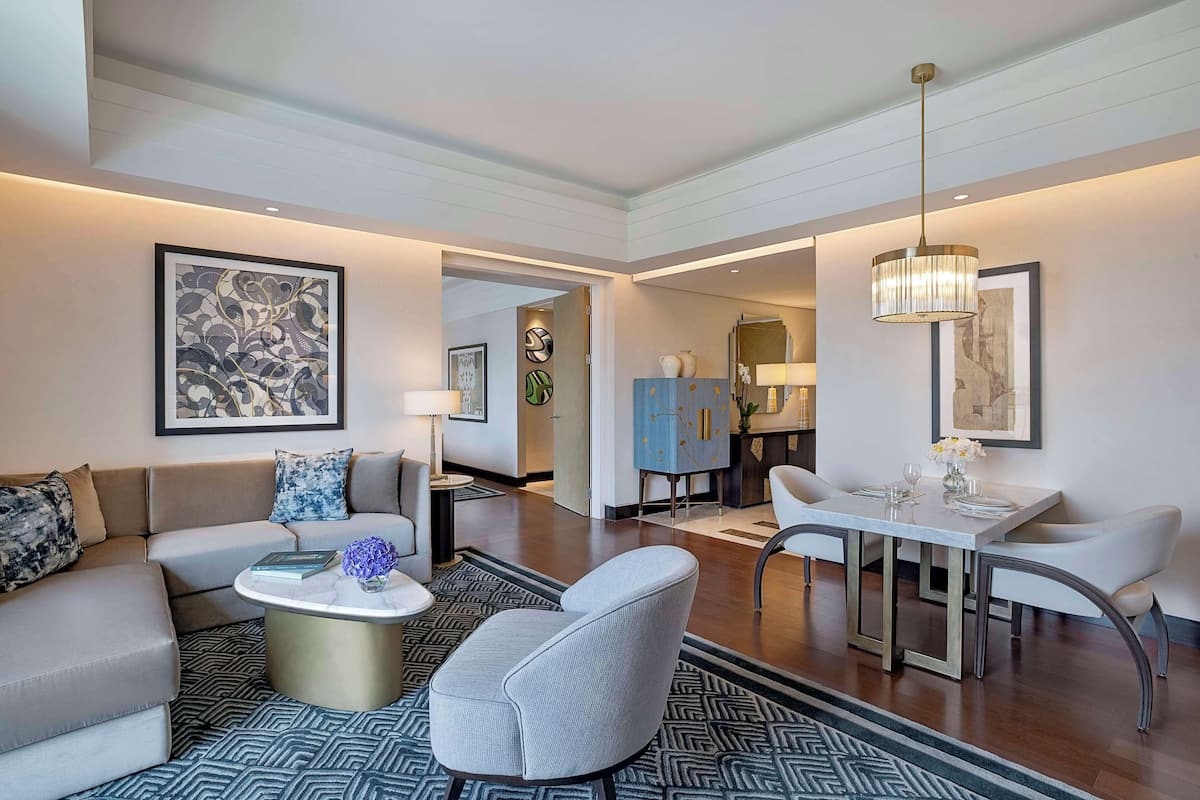 A modern living room with a sofa, armchair, coffee table, and dining area with a table and chairs.