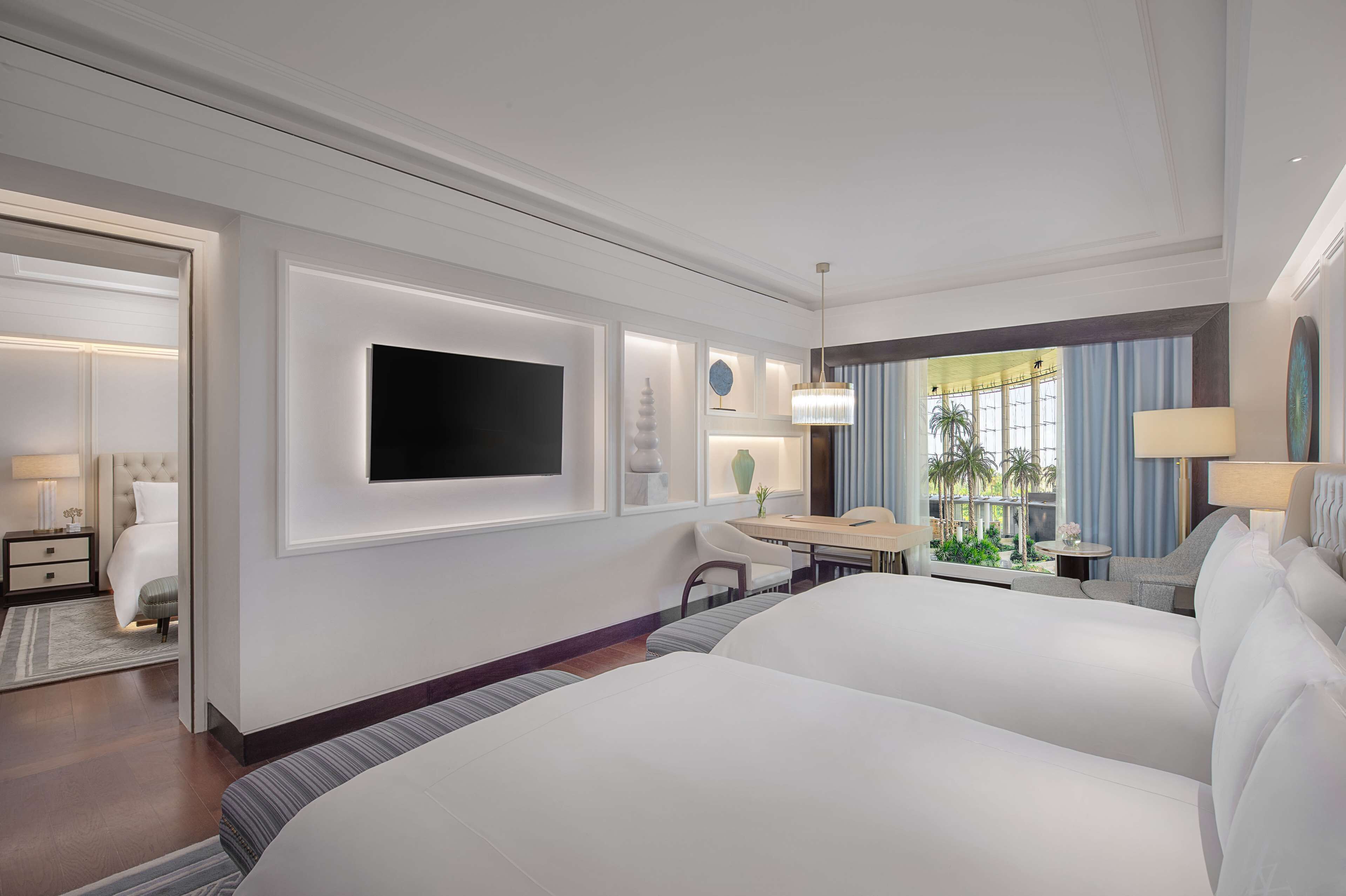 A hotel room with a large bed, a desk, a TV, and a view of the outdoors.