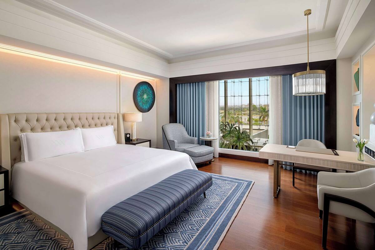 A hotel room with a large bed, a desk, a chair, and a view of the outdoors.