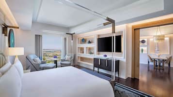 A modern hotel room with a large bed, a desk, a TV, and a dining area with a view.