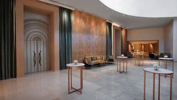 A spacious lobby with a modern design, featuring a large seating area, multiple tables, and a decorative wall with a unique pattern.