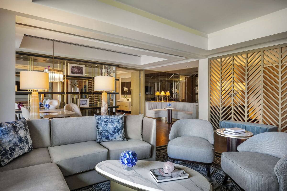 A modern hotel lobby with a sectional sofa, armchairs, a marble coffee table, and a decorative wall with a geometric pattern.