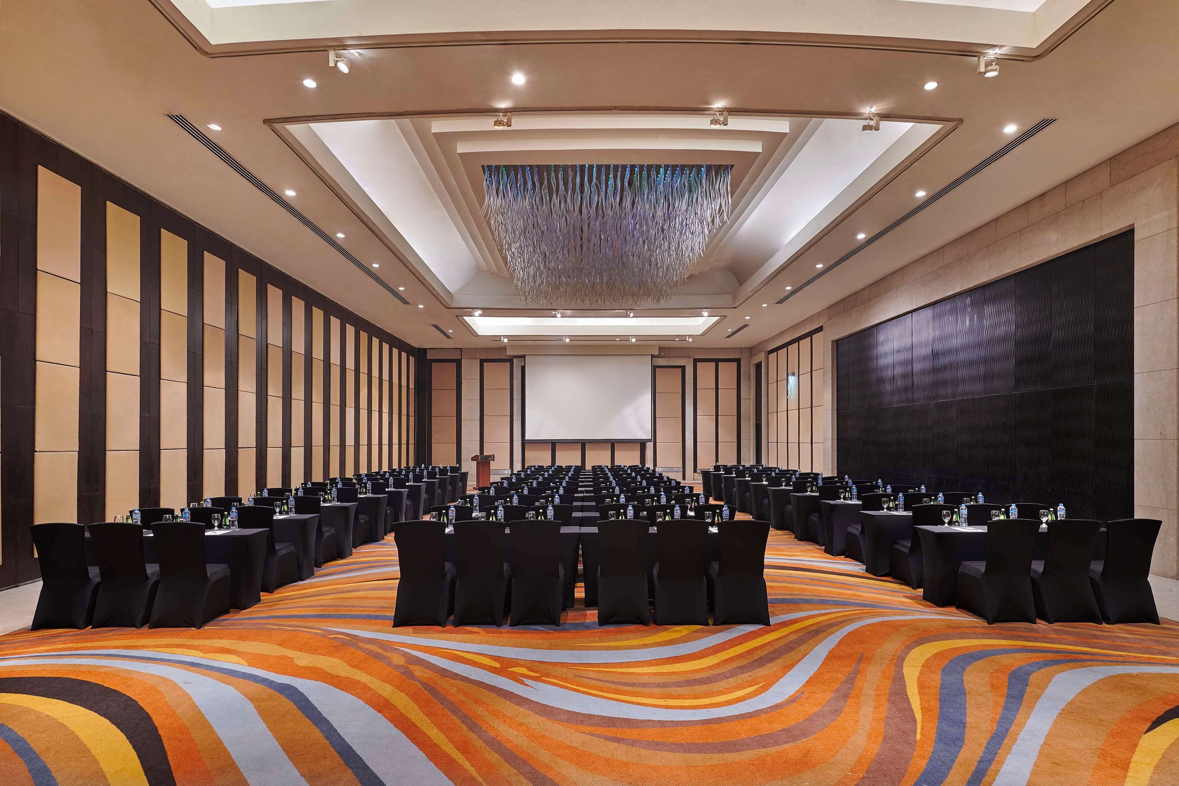 A conference room with rows of tables and chairs, a large screen, and a patterned carpet.