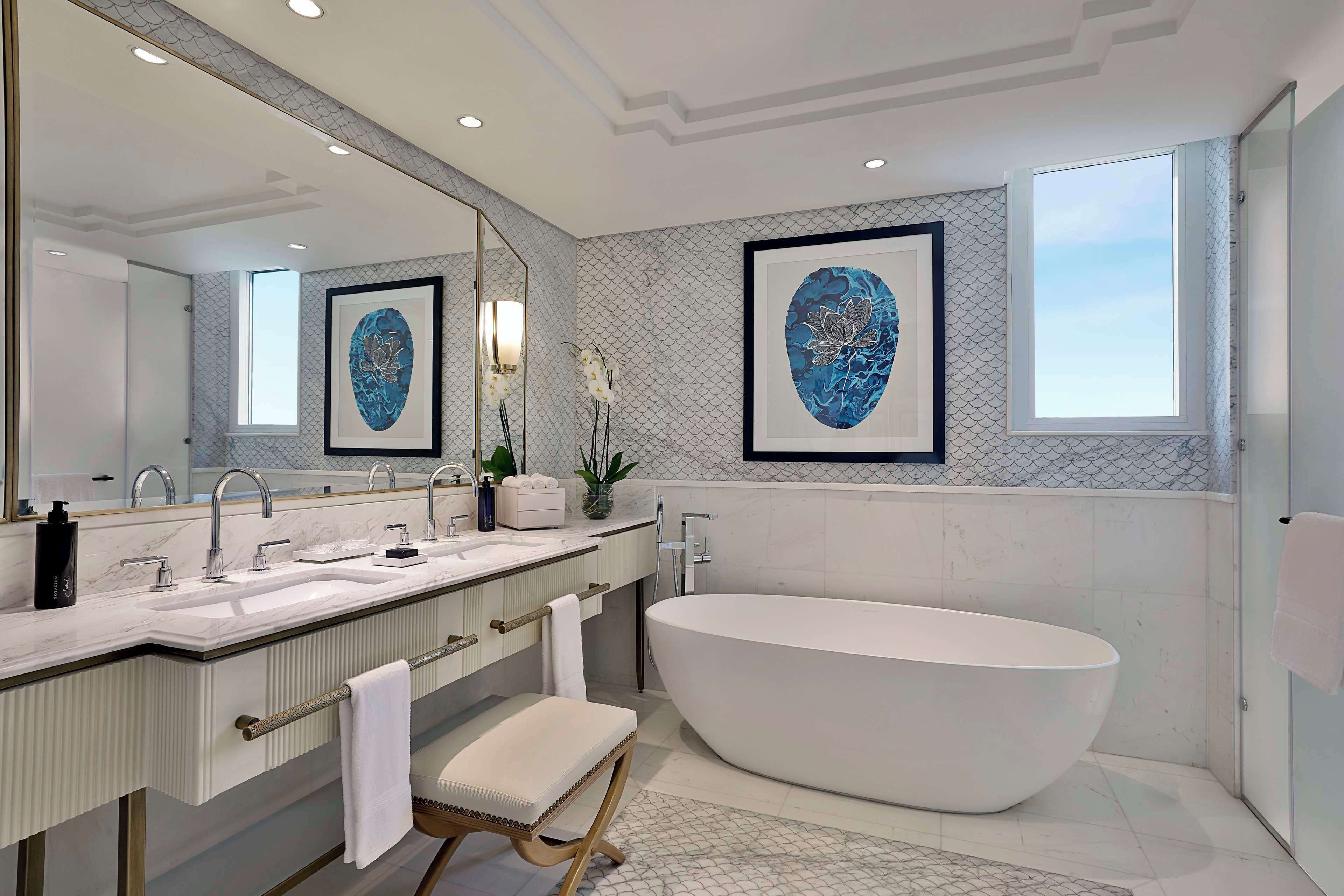 A modern bathroom with a freestanding bathtub, a large mirror, and two framed artworks on the wall.