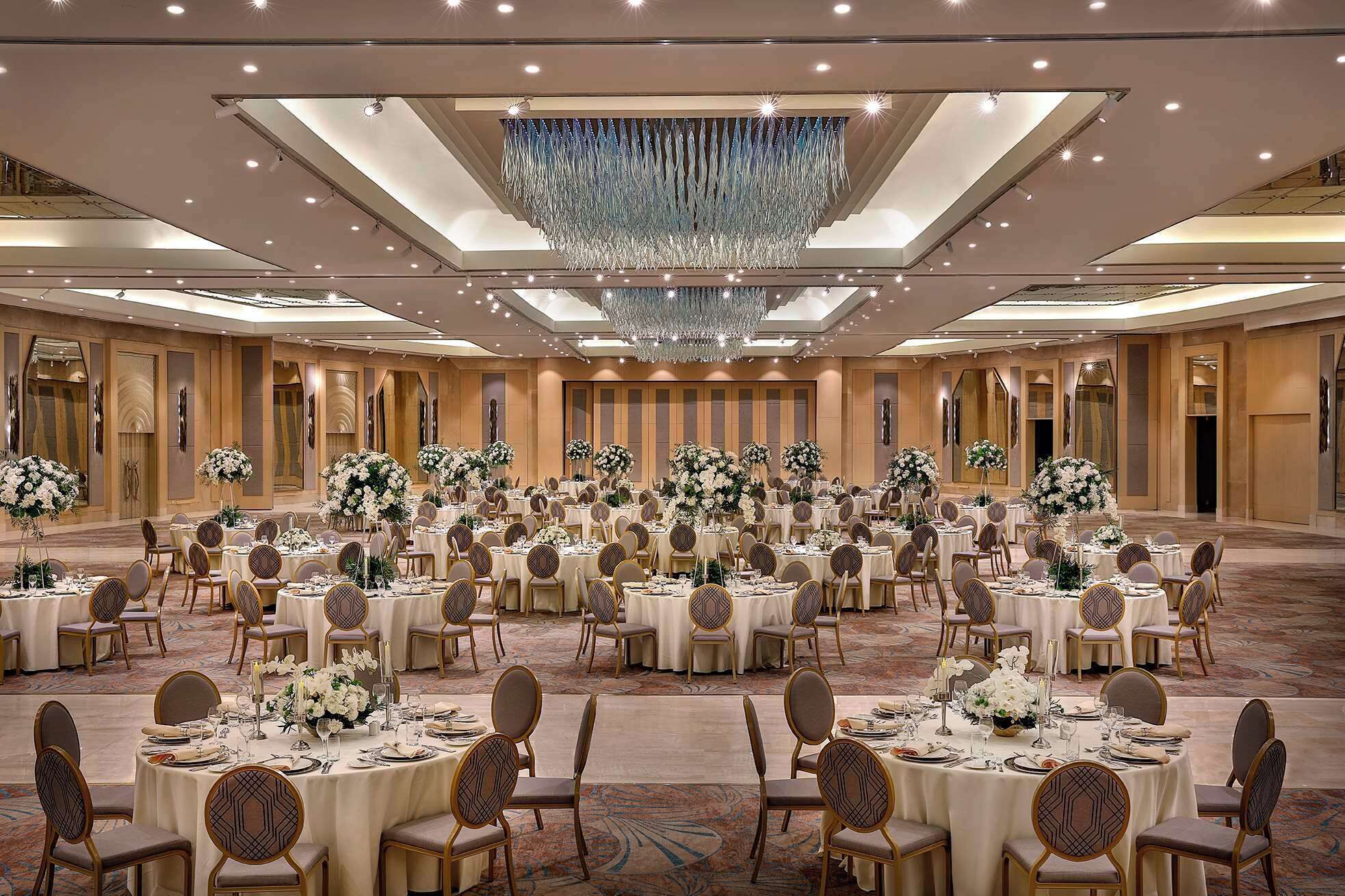 A large banquet hall with round tables, chairs, and floral centerpieces.