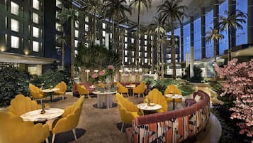 A spacious indoor atrium with high ceilings, palm trees, and yellow chairs around tables.