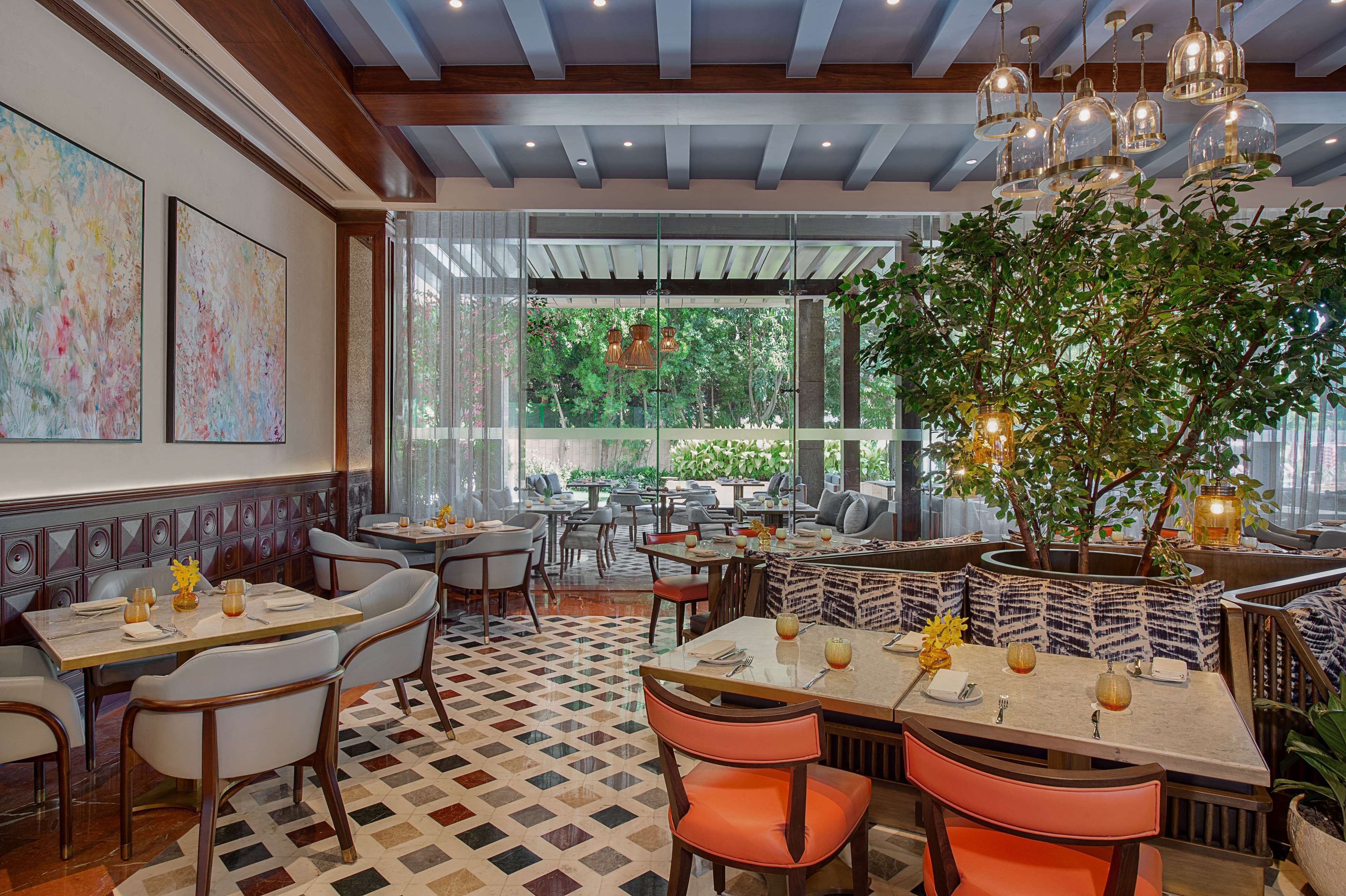 A restaurant with a checkered floor, wooden ceiling, and large windows. Tables are set with white chairs and have centerpieces.