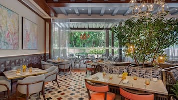 A restaurant with a checkered floor, wooden ceiling, and large windows. Tables are set with white chairs and have centerpieces.