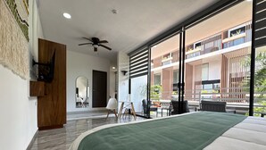 A modern hotel room with a large bed, a ceiling fan, a view of the outdoor balcony, and a wooden wardrobe.