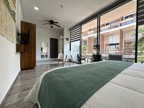 Une chambre d’hôtel moderne dotée d’un grand lit, d’un ventilateur de plafond, d’une vue sur le balcon extérieur et d’une armoire en bois.