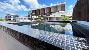 A swimming pool with a tiled edge, a modern building with vertical wooden slats, and a clear blue sky.
