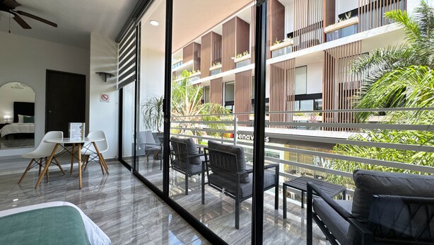 A modern hotel room with a balcony, a dining area, and a view of the building's exterior.