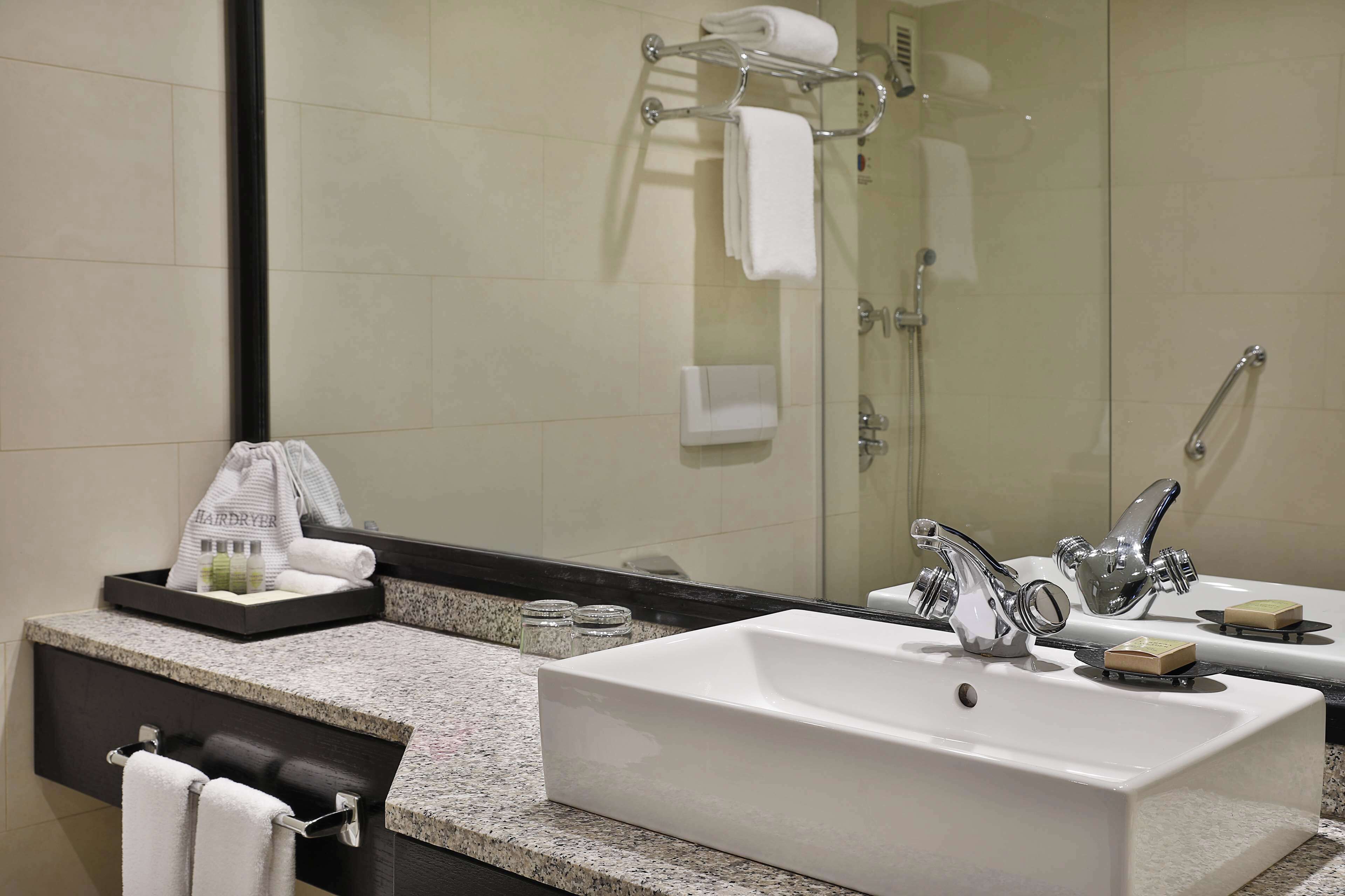 A bathroom with a large mirror, two sinks, a towel rack, and a shower area.