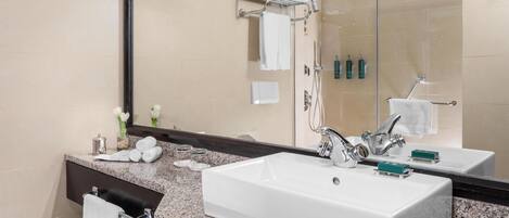 A bathroom with a large mirror, two sinks, a towel rack, and a shower area.