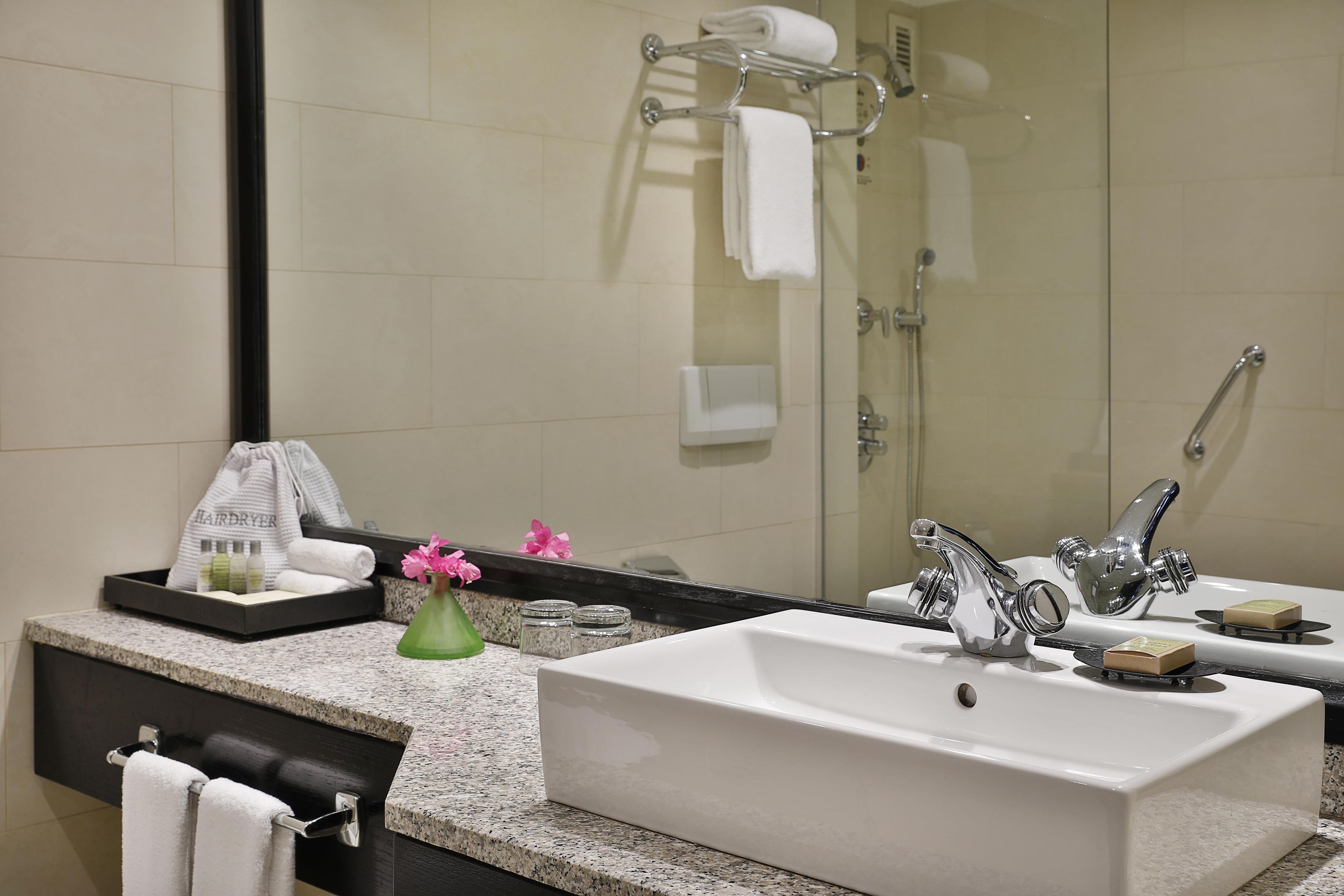 A bathroom with a large mirror, a sink, a shower, and a towel rack.