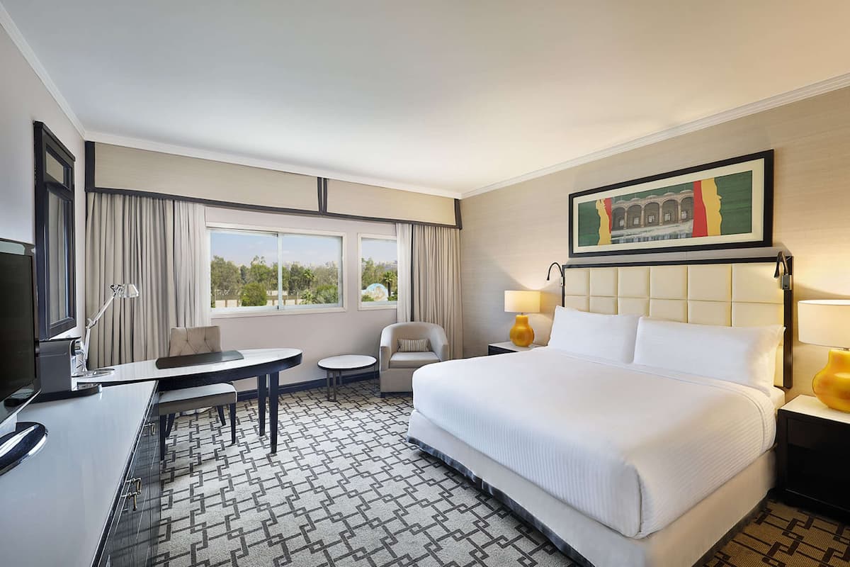 Quarto de hotel com uma cama grande, uma escrivaninha, uma cadeira, uma televisão e uma janela com cortinas.