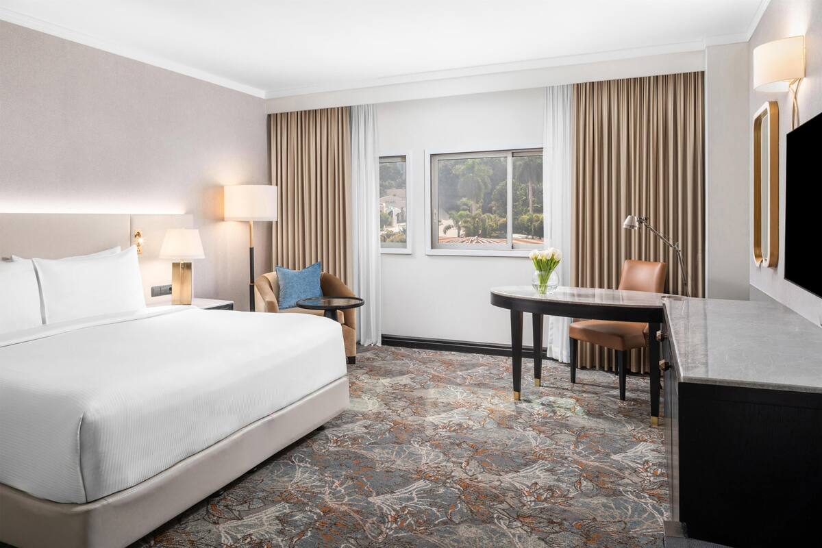 Quarto de hotel com uma cama grande, uma escrivaninha, uma cadeira, uma mesa e uma televisão.