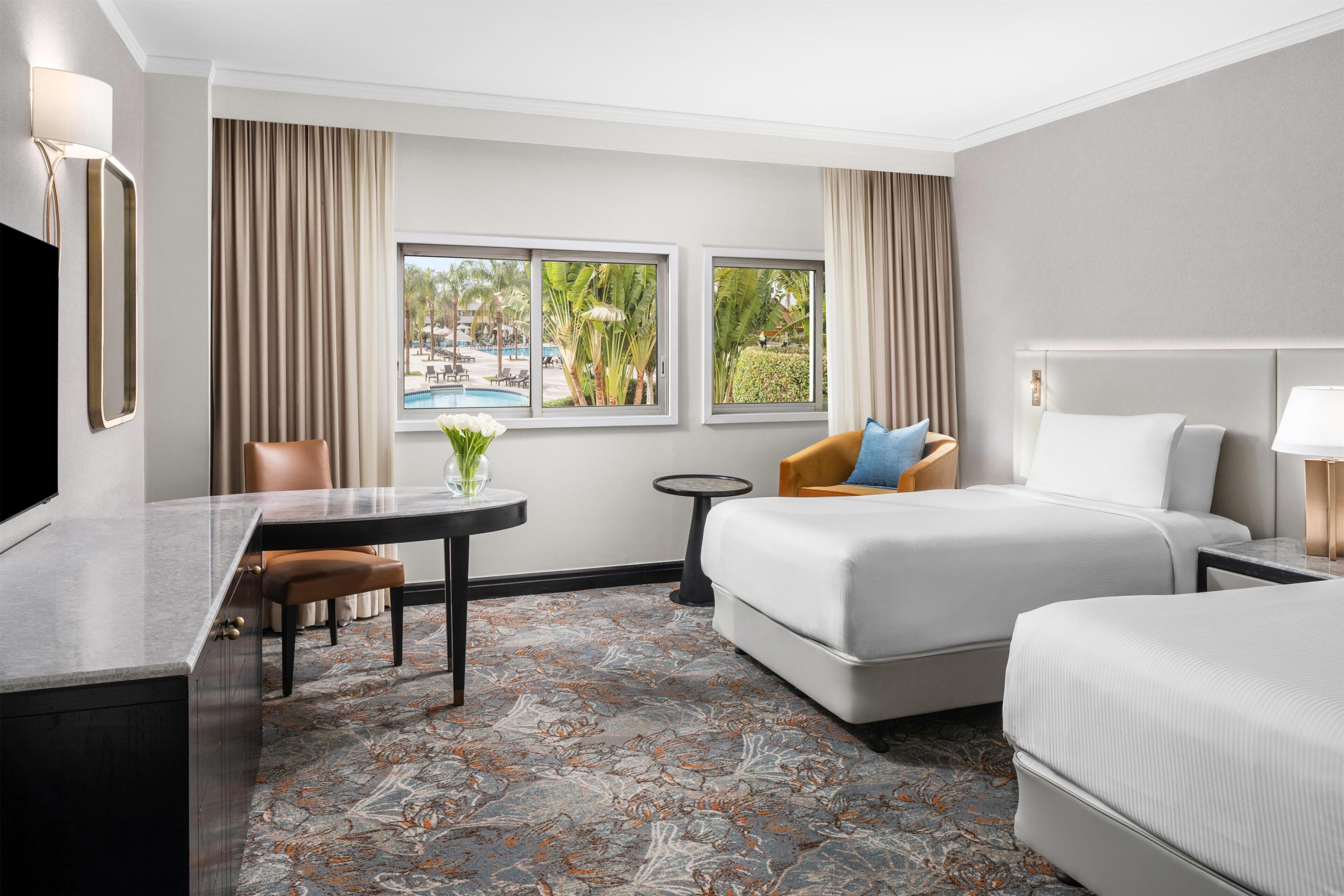 Une chambre d’hôtel avec un lit, un bureau, une chaise, une petite table et une vue sur la piscine.