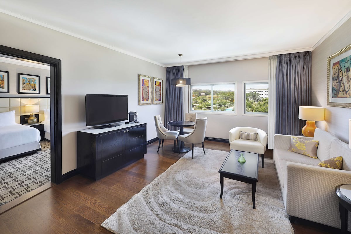 Quarto de hotel com cama, televisão, escrivaninha, poltrona, sofá e vista para o exterior.