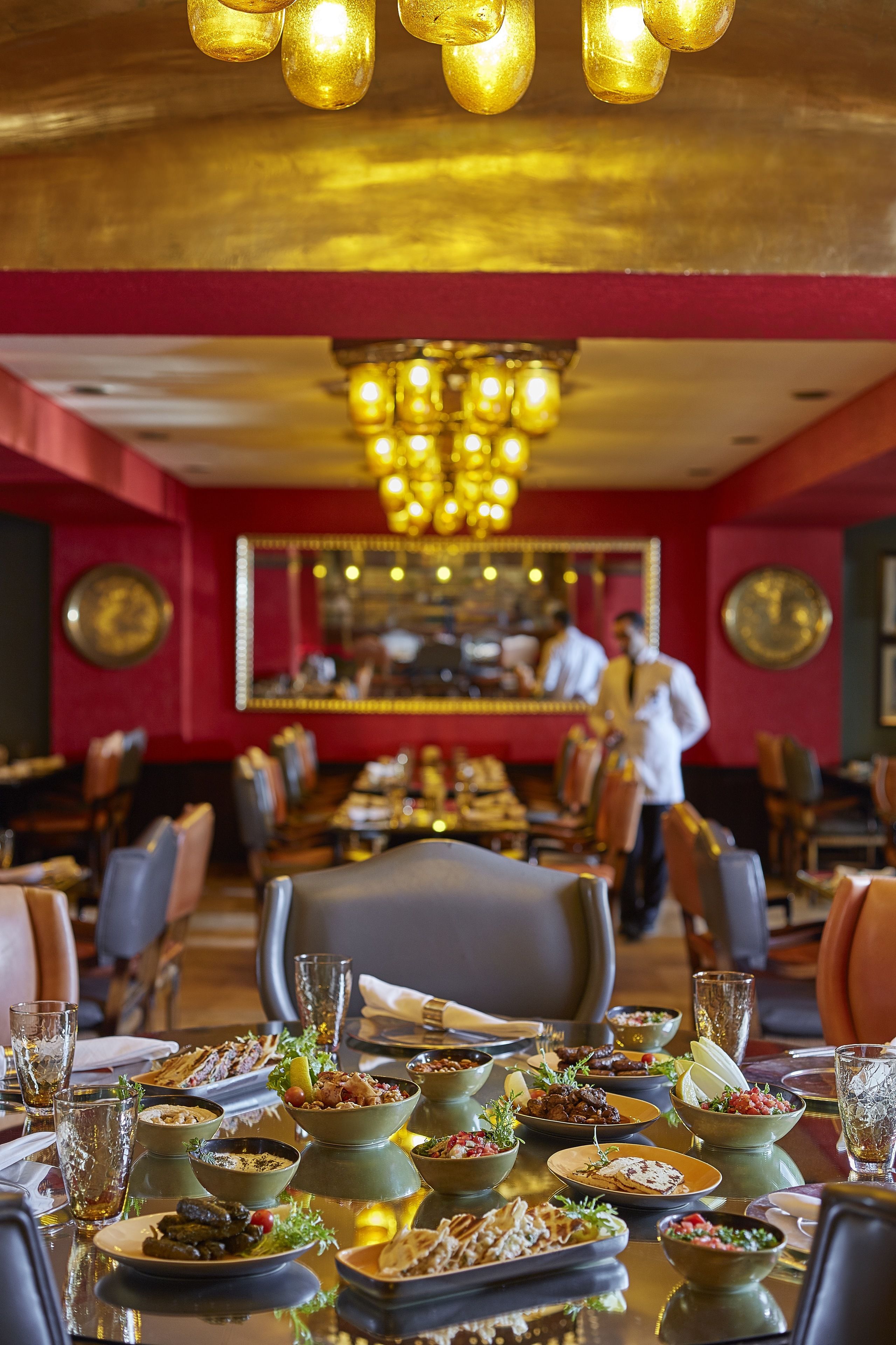 Un restaurante con una larga mesa de comedor dispuesta con diversos platos, una araña y un espejo grande en la pared.