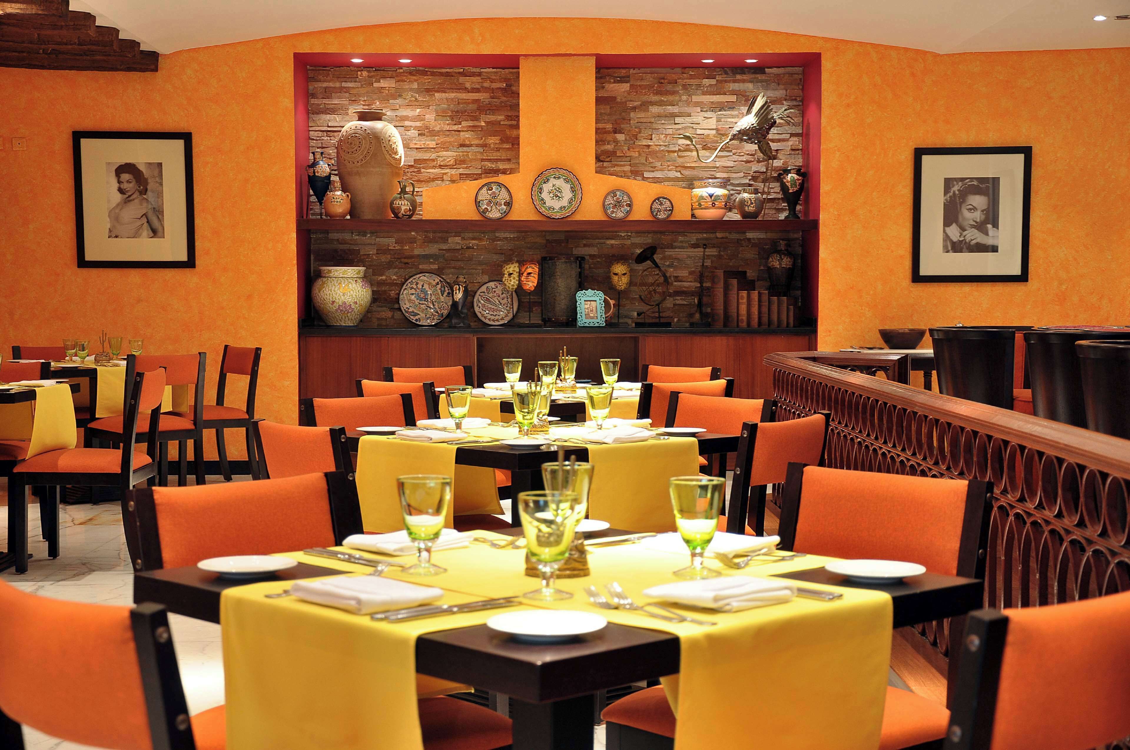 A restaurant with orange chairs and tables, a brick wall with decorative plates, and framed pictures on the walls.