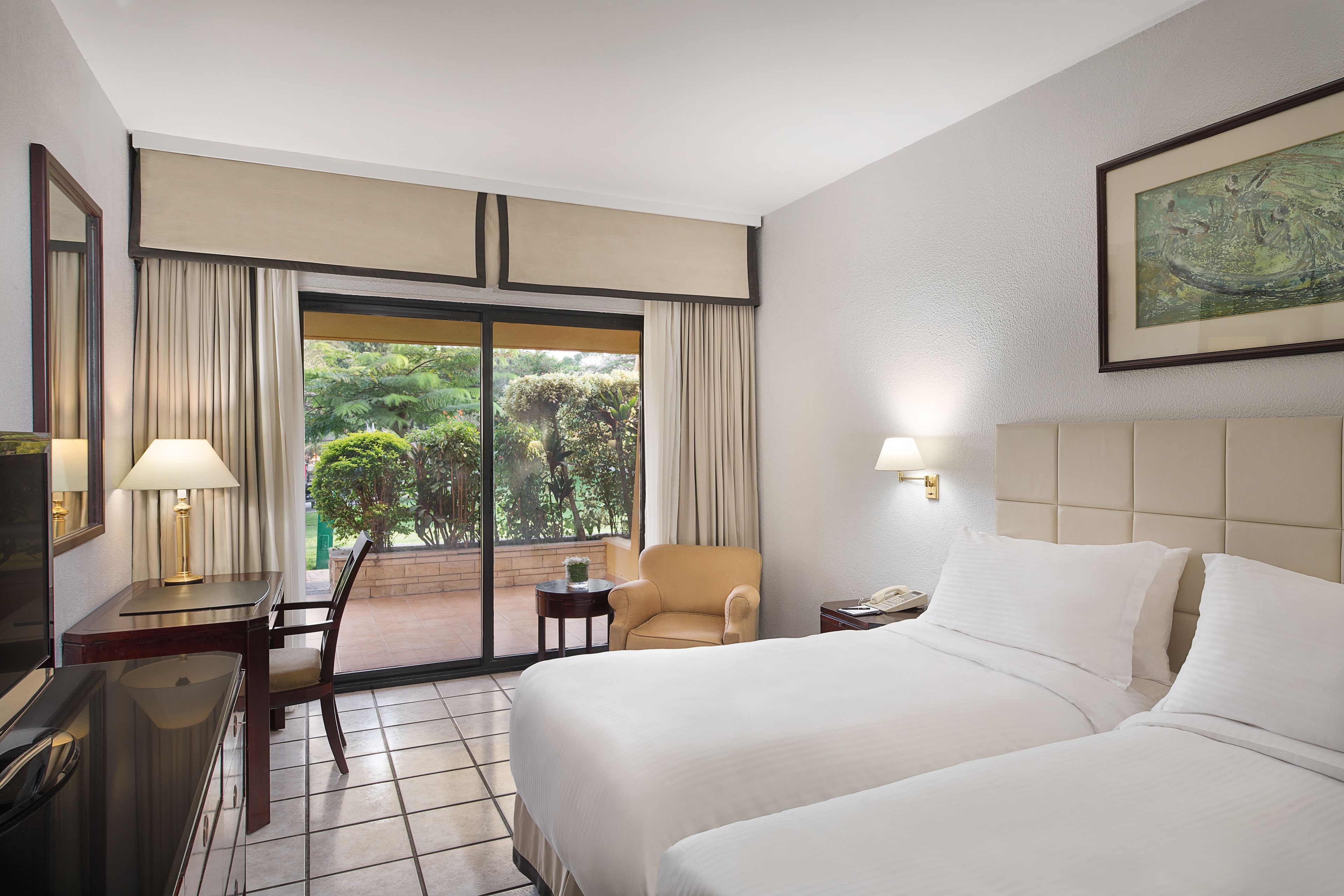 A hotel room with two beds, a desk, a chair, a TV, and a window with curtains.
