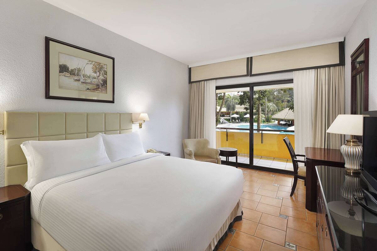 Quarto de hotel com uma cama grande, uma escrivaninha, uma cadeira, uma televisão e vista para uma piscina.