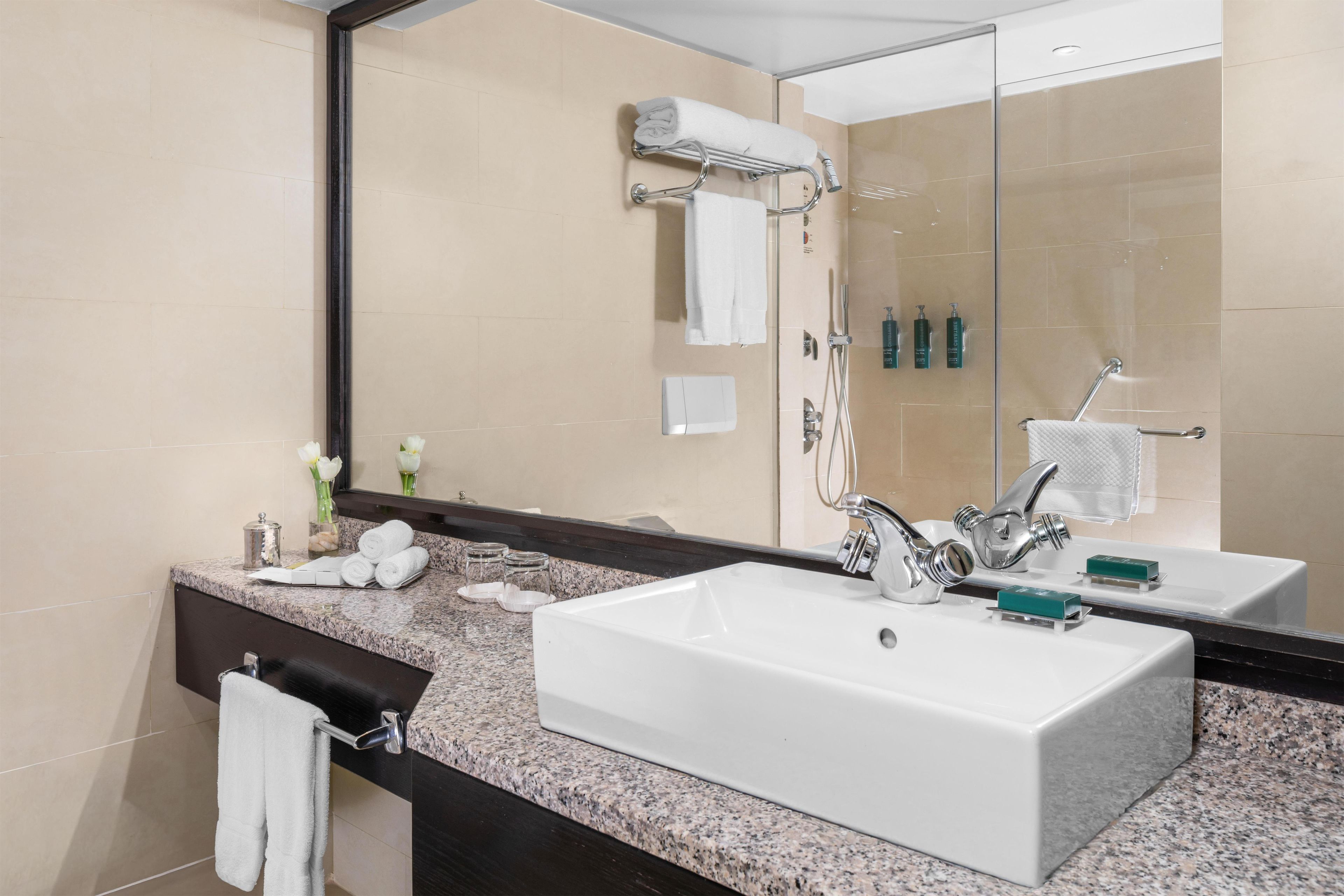 A bathroom with a large mirror, two sinks, a towel rack, and a shower area.