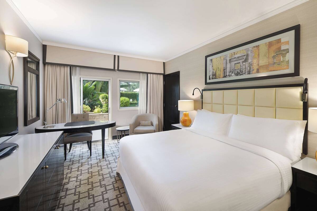 Quarto de hotel com uma cama grande, uma escrivaninha com cadeira, televisão e um quadro na parede.