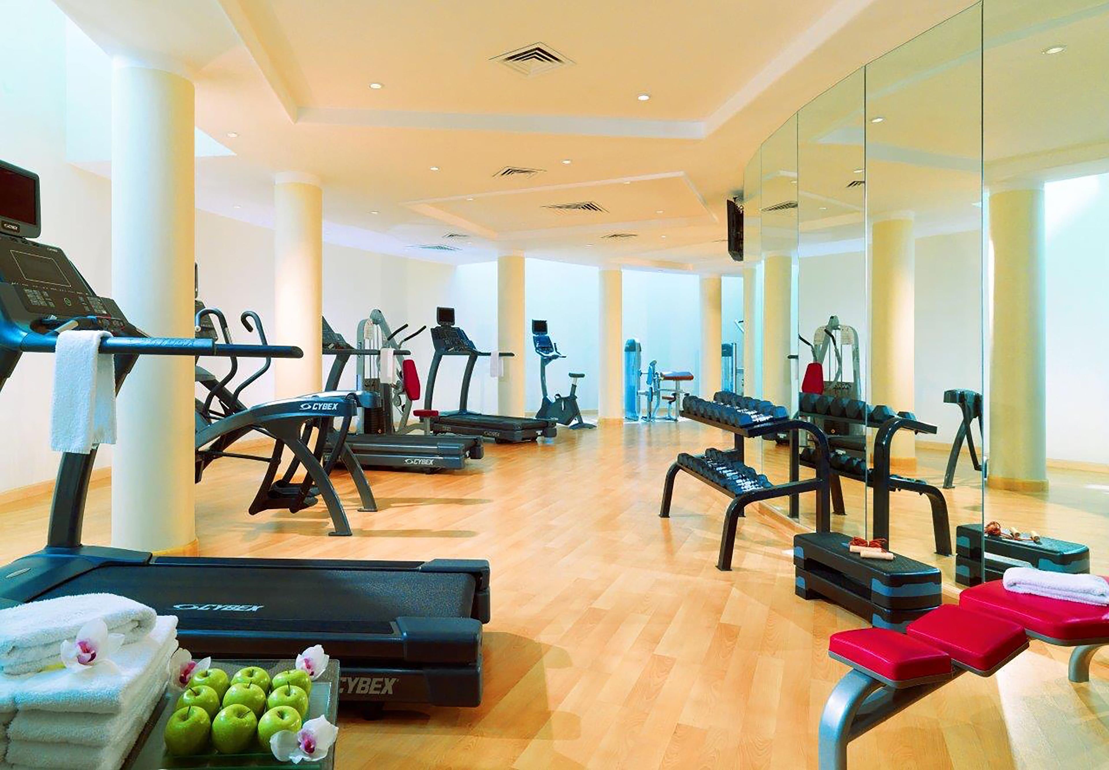 A gym with cardio machines, weight benches, and a mirror wall.