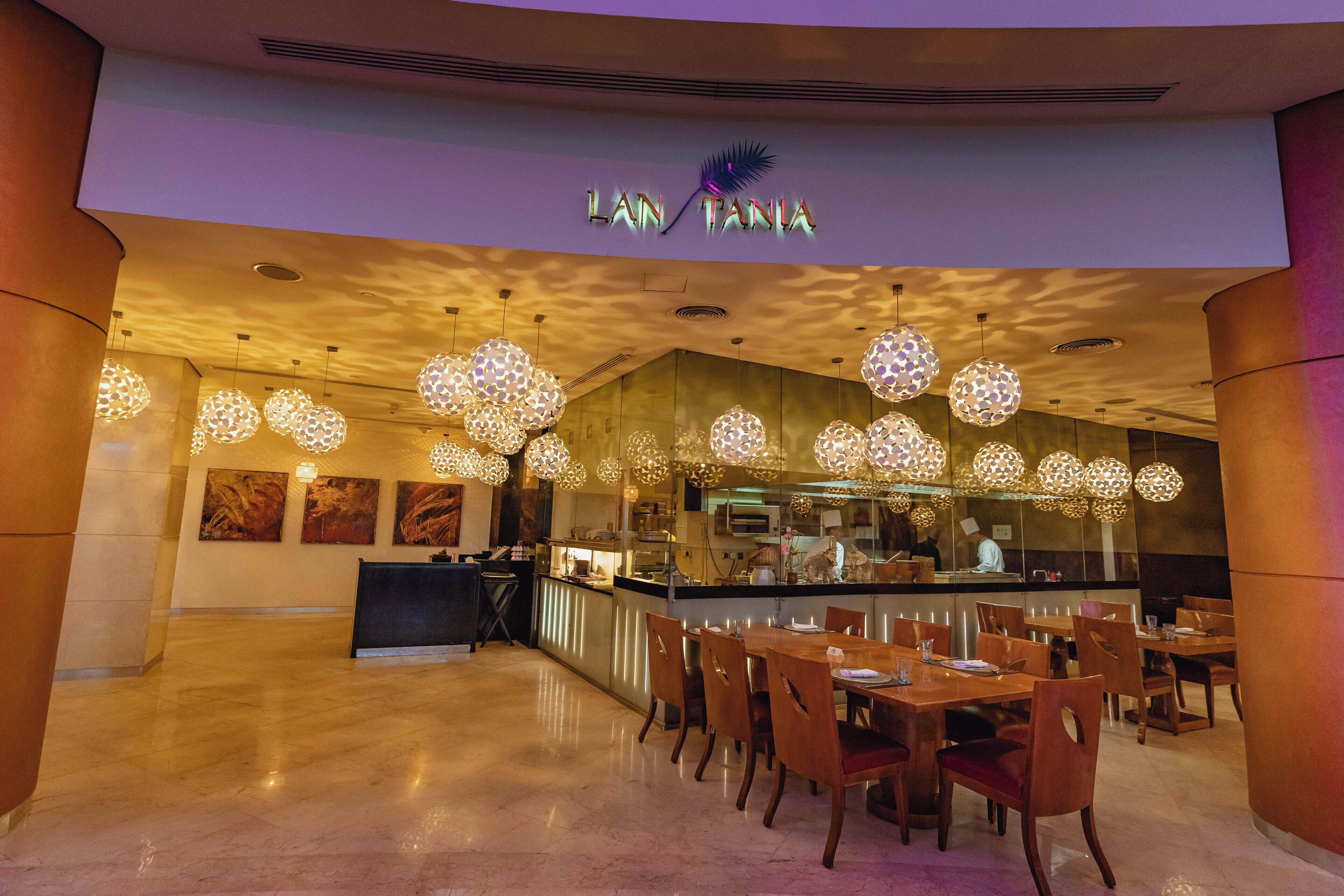 Un restaurant au décor moderne, comprenant un bar, des tables et des chaises en bois, ainsi que des luminaires décoratifs suspendus.