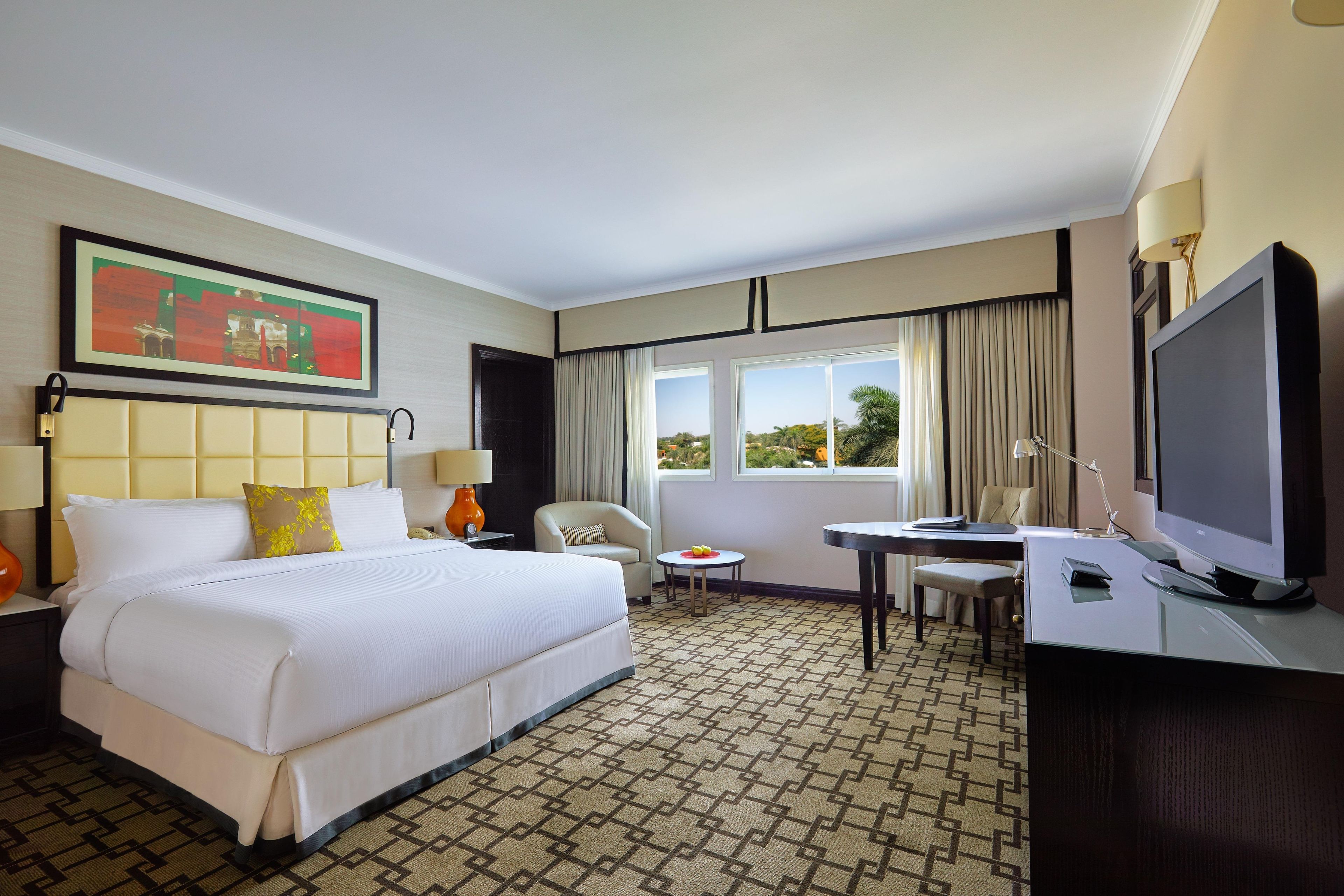 Habitación de hotel con cama, escritorio, silla, televisión y ventana con cortinas.