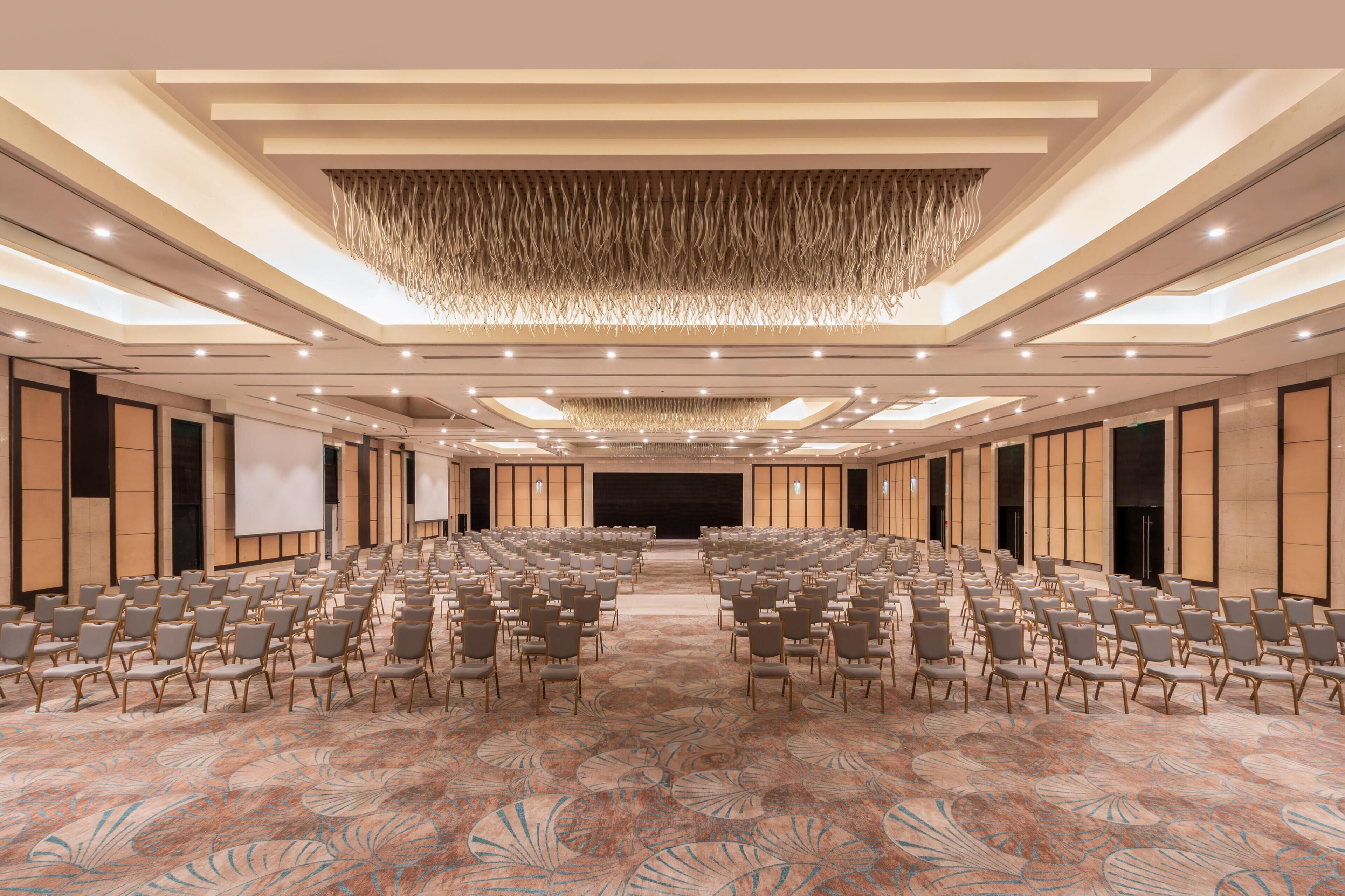 A large conference room with rows of chairs, a stage, and a patterned carpet.