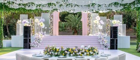 Un espacio al aire libre para eventos, con escenario, arreglos florales y asientos.