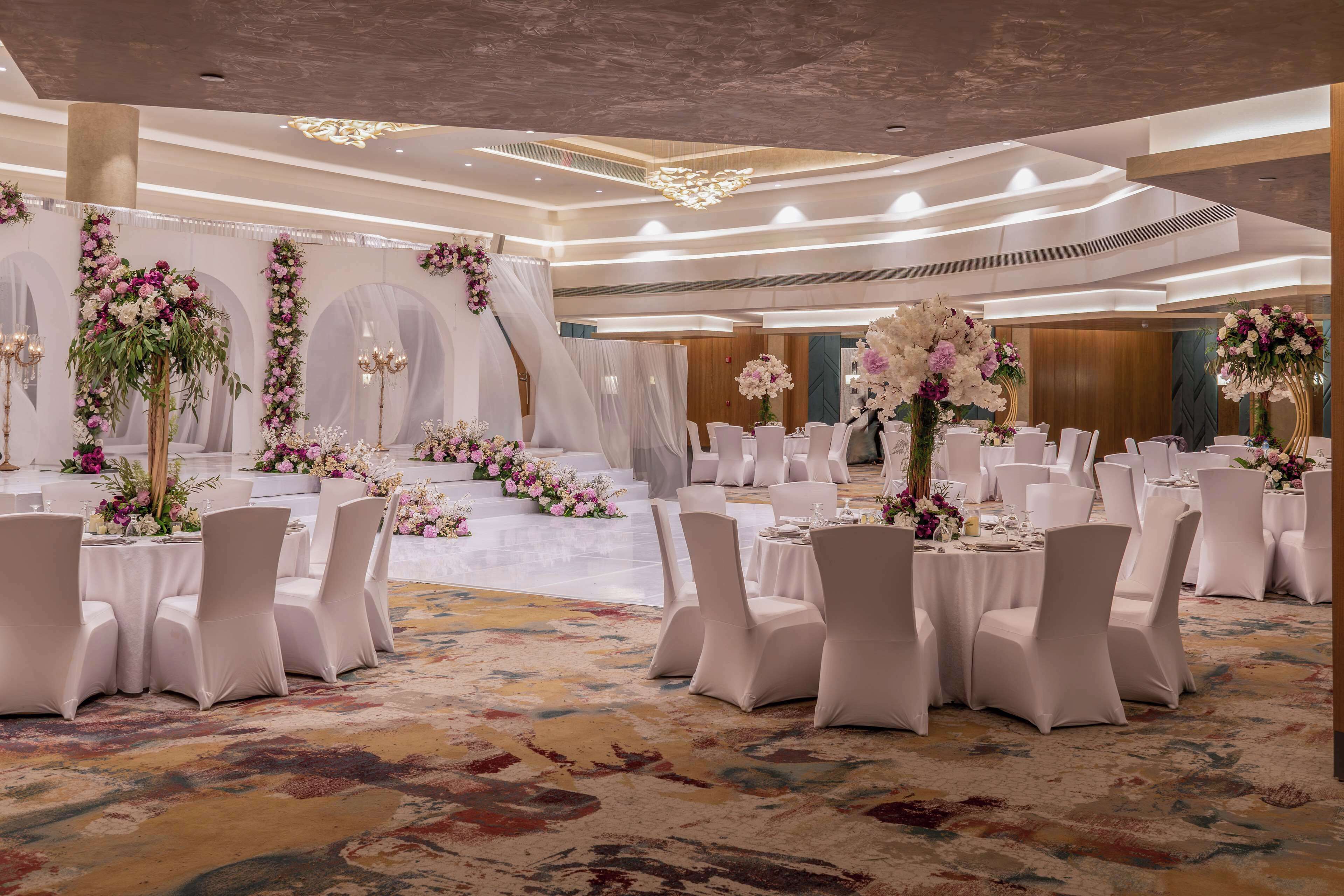A banquet hall with round tables, white chairs, and floral centerpieces.