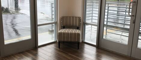 Habitación de esquina con una silla a rayas, ventanas amplias y suelo de madera.
