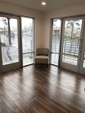 A corner room with a striped chair, large windows, and wooden flooring. - Castaway Motel (Orange)
