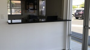 An interior space with a dark wood floor, a counter with a computer, and a view of the street through a glass door. - Castaway Motel (Orange)