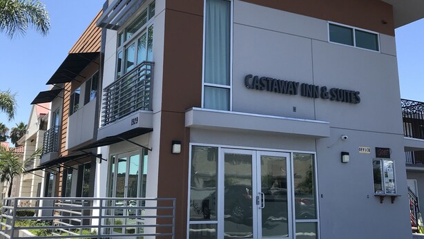 A two-story building with a sign for "CASTAWAY INN & SUITES" and a visible office entrance. - Castaway Motel (Orange)