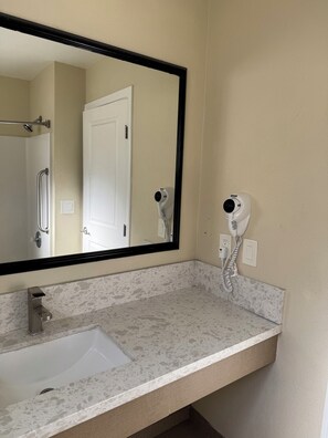 A bathroom with a sink, mirror, and two hair dryers mounted on the wall. - Castaway Motel (Orange)