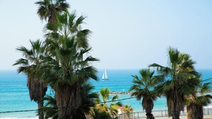 A coastal view with palm trees, a sailboat, and a beach in the background. - Panoramic Ocean View 1 min From the Sea (Tel Aviv)